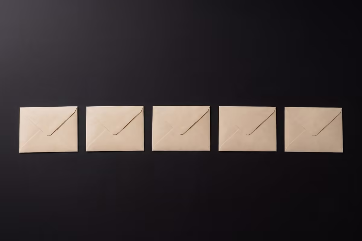Five identical blank sealed envelopes in an evenly spaced row on a dark surface