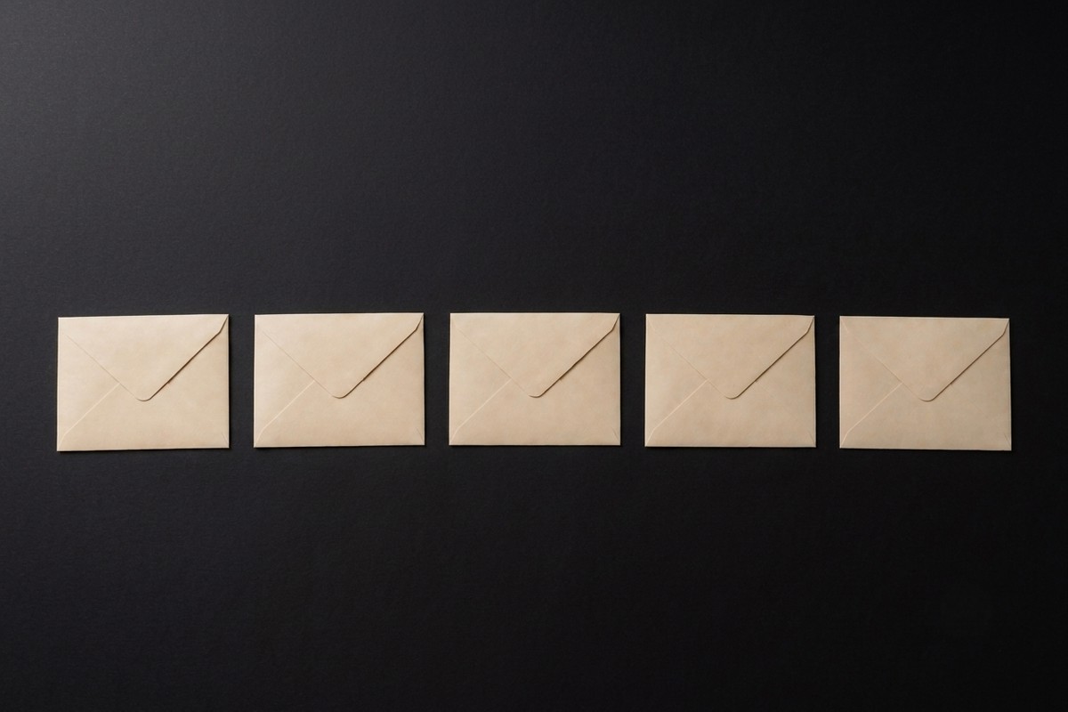 Five identical blank sealed envelopes in an evenly spaced row on a dark surface